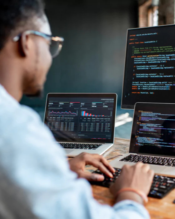 Person som skriver vid ett skrivbord med flera datorskärmar som visar kod och dataanalys, använder C++ för utvecklare för att förbättra prestanda och effektivisera programmeringsuppgifter.