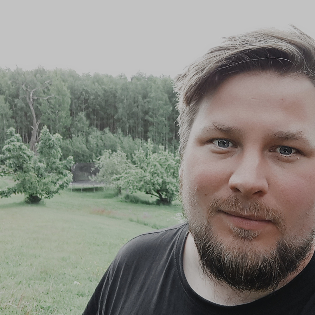En skäggig man med kort hår står utomhus på ett gräsbevuxet fält med träd i bakgrunden och funderar över idéer för produktionsutveckling.