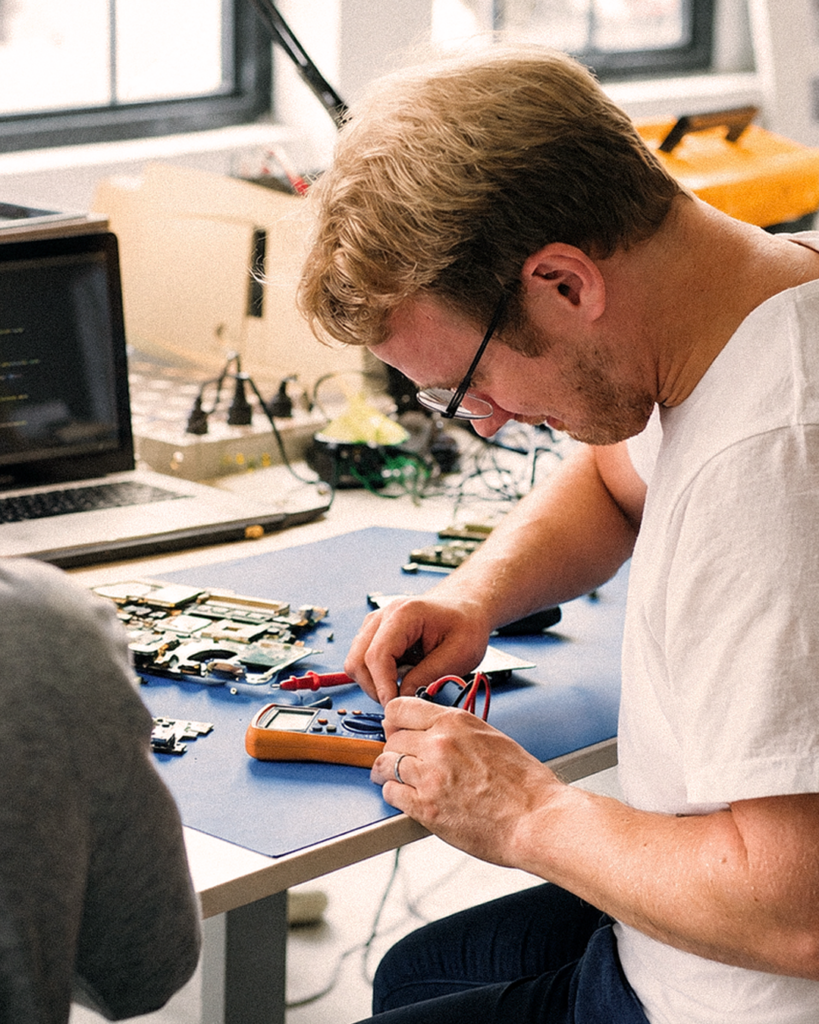 En man som använder en multimeter för att testa elektroniska komponenter vid en arbetsbänk i ett ljust, modernt laboratorium, vilket visar på den precision och uppmärksamhet på detaljer som kännetecknar en avancerad mjukvaruutvecklare.