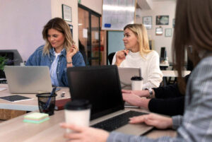 Fyra personer sitter vid ett bord med bärbara datorer och kaffekoppar, engagerade i en livlig diskussion om annonsering i sociala medier i en kontorsmiljö.