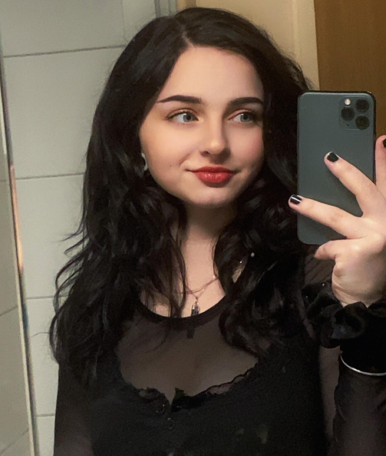En kvinna med långt mörkt hår, som arbetar som köttförädlare, tar en spegelselfie iklädd svart topp och rött läppstift.