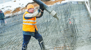 Betongarbetare i en orange väst och hjälm som häller betong på en byggarbetsplats med armeringsjärn.