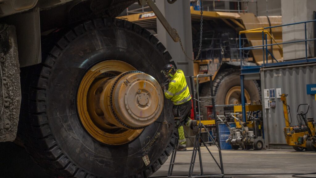 En arbetare i säkerhetsutrustning inspekterar ett stort industrifordonsdäck i ett lager.