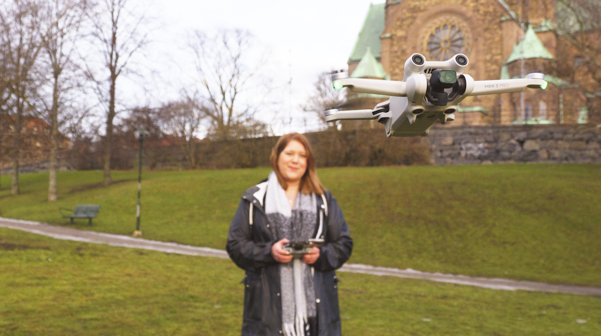 En drönarpilot navigerar skickligt en flygande drönare i parken och fångar hisnande vyer av en historisk byggnad i bakgrunden.