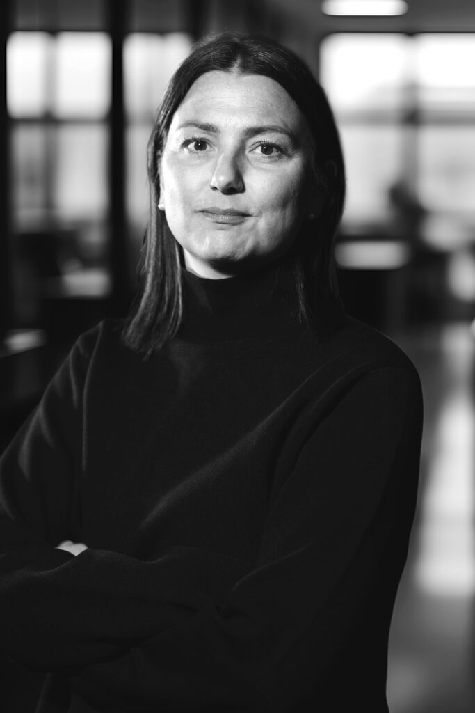 En person i svart turtleneck står med armarna i kors i ett svagt upplyst rum.