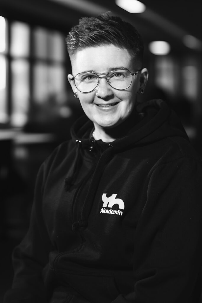 Person med glasögon och kort hår som ler i en hoodie med 