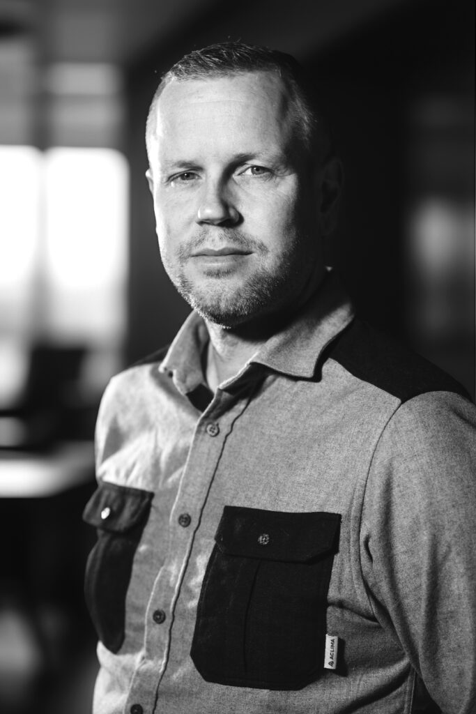 Man i en tvåfärgad skjorta poserar i mjukt fokus svart och vitt och tittar på kameran.