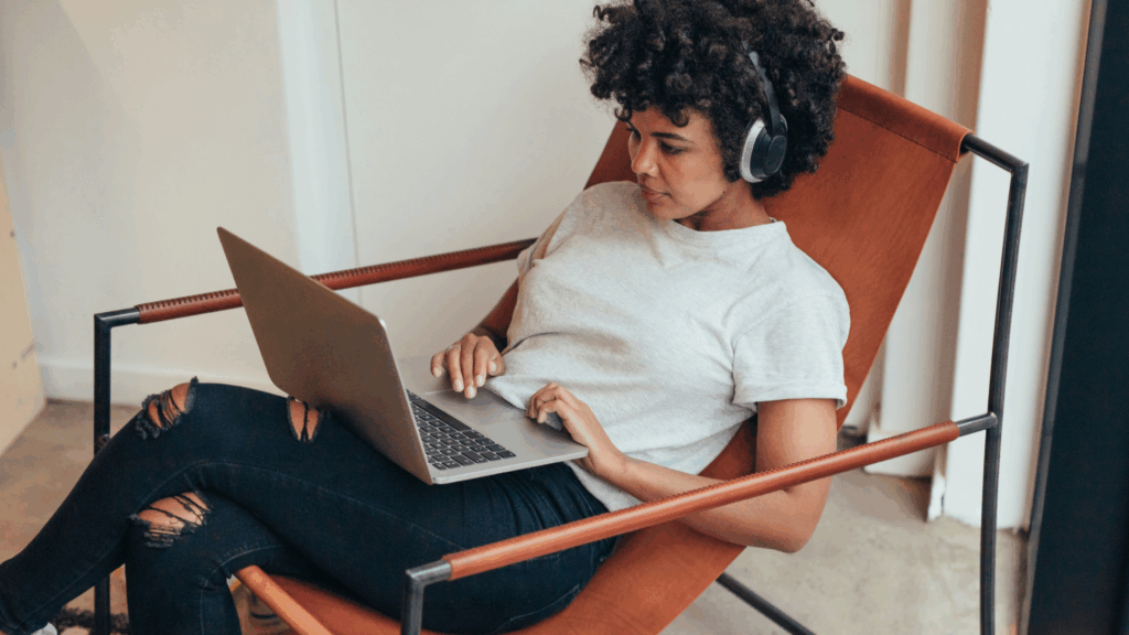 Person med hörlurar sitter i en stol, använder en bärbar dator och verkar fokuserad och avslappnad-kanske med inspiration från våra bästa tips för bra studieteknik.
