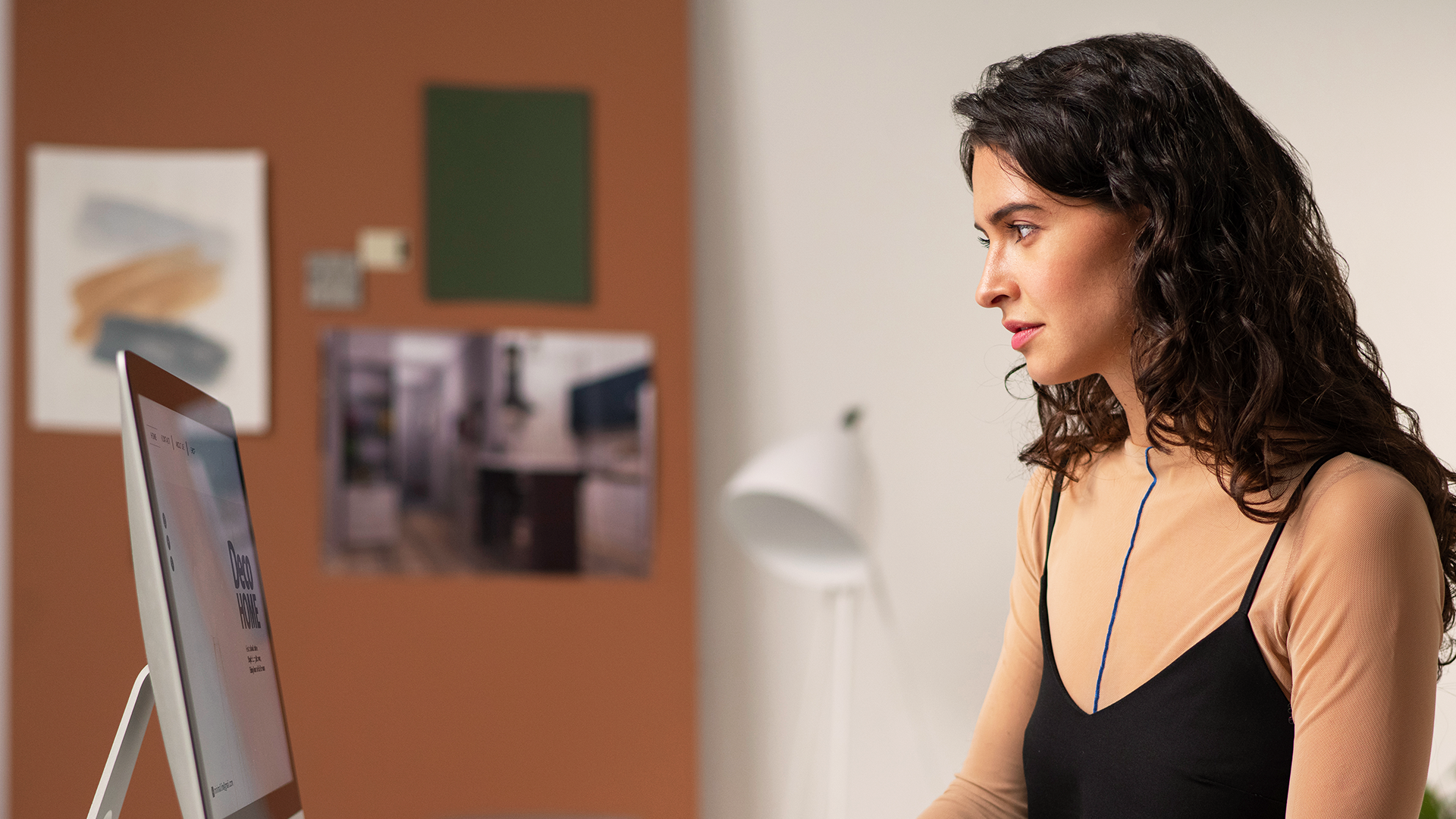 Kvinna med lockigt hår arbetar vid en stationär dator i en modern, väl upplyst kontorslokal.