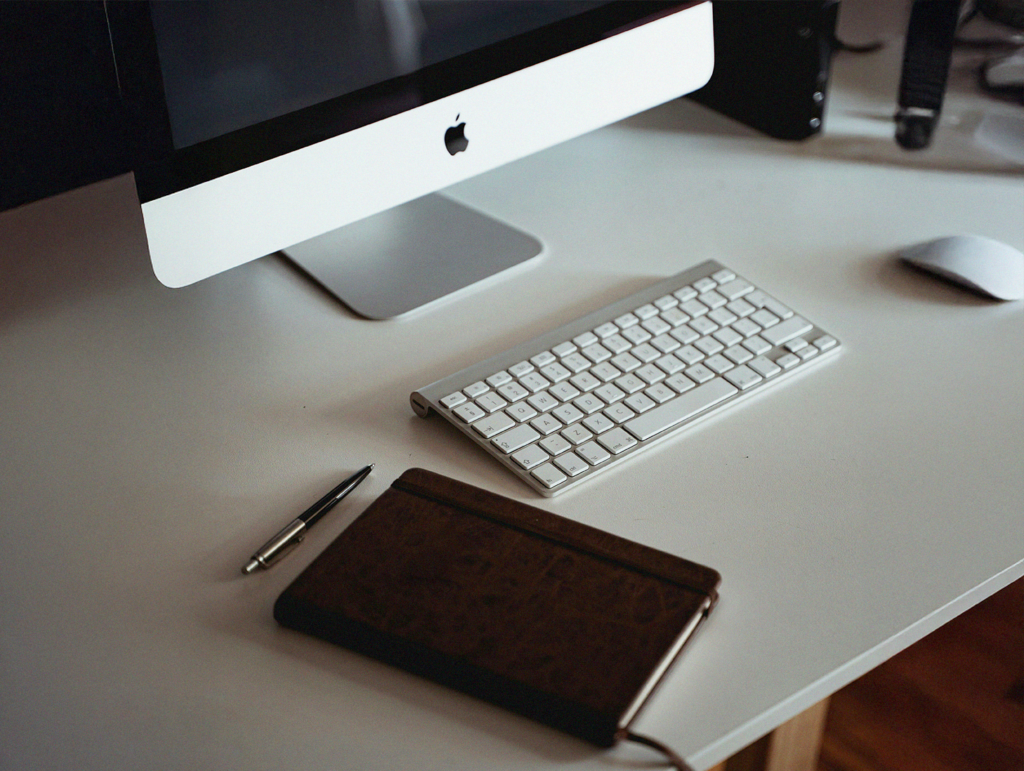 En stationär dator, tangentbord, mus, penna och anteckningsblock på ett vitt skrivbord - perfekt för att studera eller arbeta med uppgifter för yrkeshögskolan.