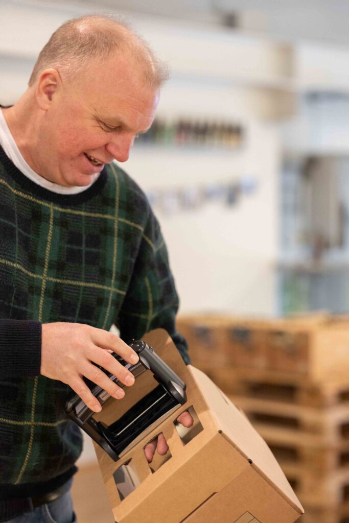 En man ler när han skannar en kartong med en streckkodsläsare på ett lager under Kurs: Hållbar affärsutveckling inom gårdsförsäljning.