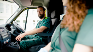 En ambulanssjukvårdare sitter i förarsätet i en ambulans och tittar på en kollega i passagerarsätet.