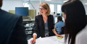 Leende kvinna i affärskläder leder ett möte med kollegor runt ett bord på ett modernt kontor.