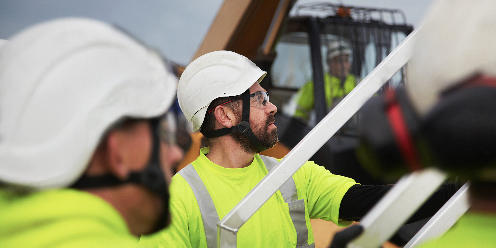 Byggnadsarbetare i skyddsutrustning och hjälm arbetar tillsammans på en byggarbetsplats med maskiner i bakgrunden.