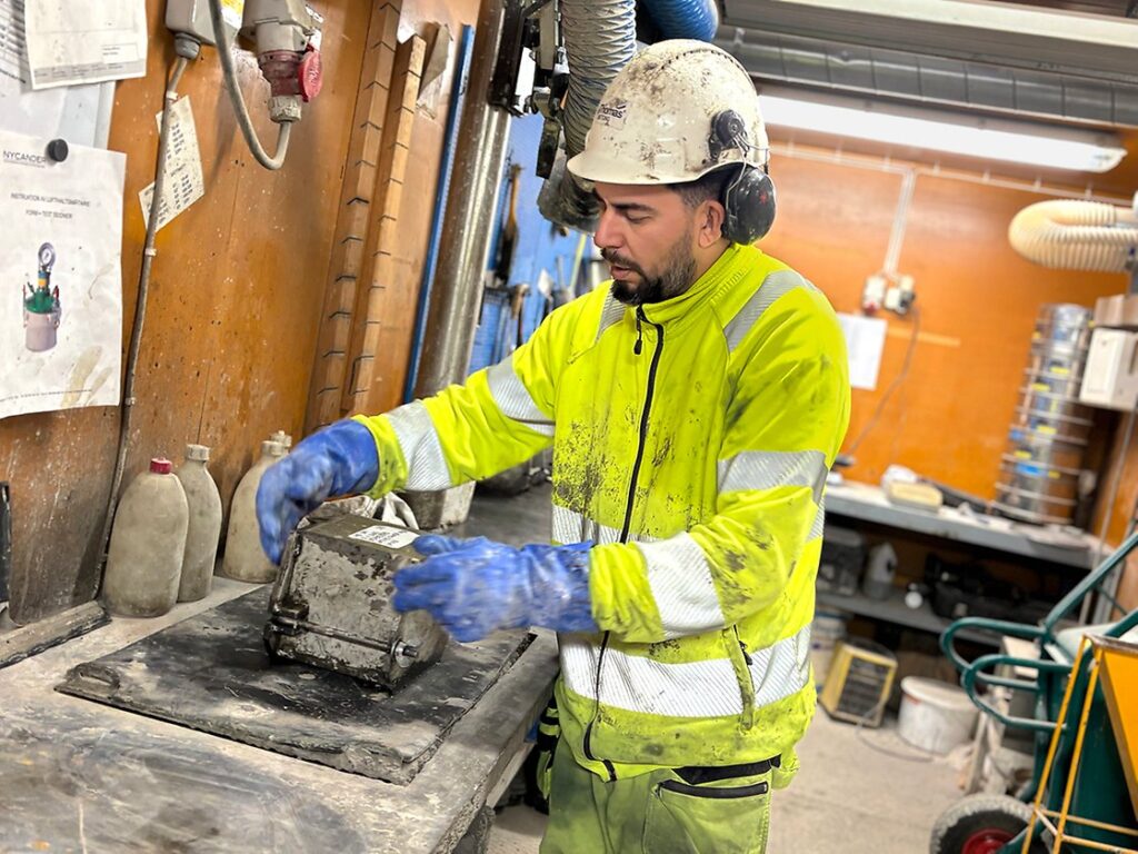 En arbetare i hjälm och skyddsjacka hanterar utrustning i en industriverkstad i Nationella yrkesutbildningen betongarbetare som nu ska börja YH-utbildningen Betongingenjör.