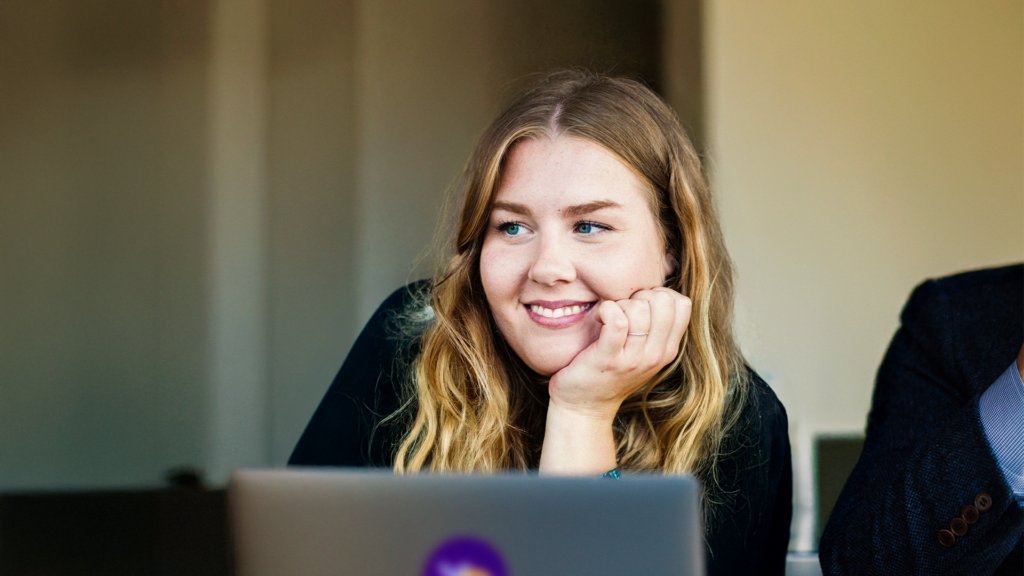 En kvinna ler med handen på hakan och utstrålar värme och entusiasm när hon välkomnar gästerna till öppet hus.