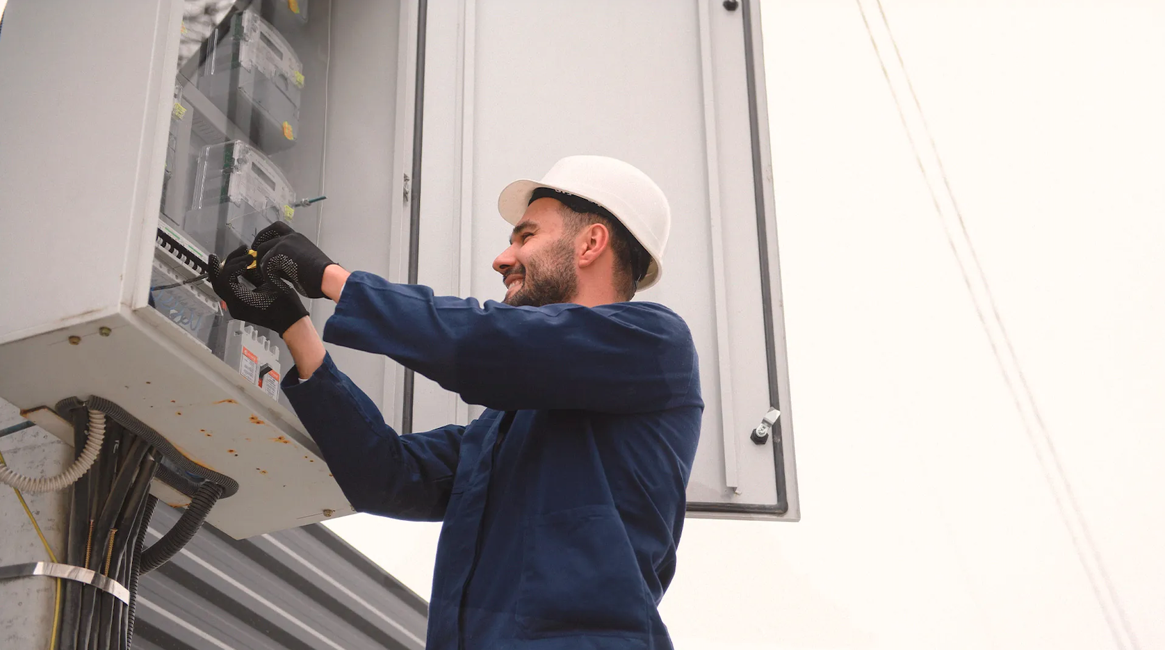 Elektriker i blå uniform och skyddshjälm arbetar på en öppen elcentral utomhus, som YH-Akademin beviljas nya utbildningar inom YH-flex.