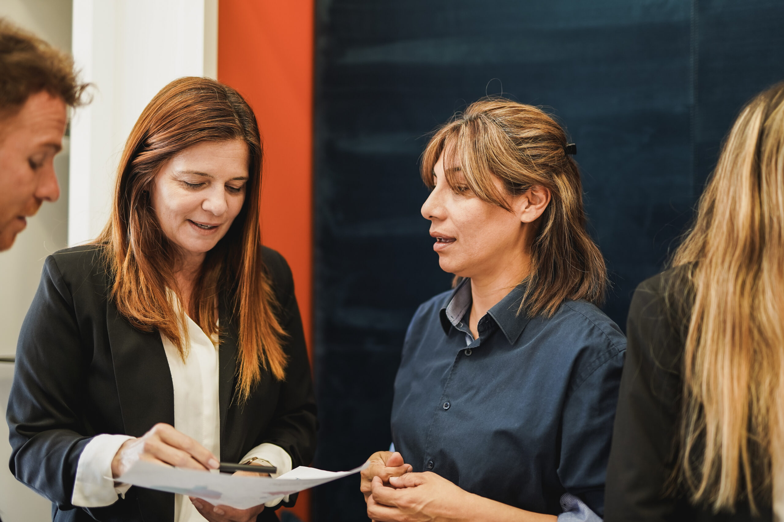 Två kvinnor går igenom dokument tillsammans och diskuterar Learning & Development för HR, medan en annan person står i närheten, delvis utanför bild.