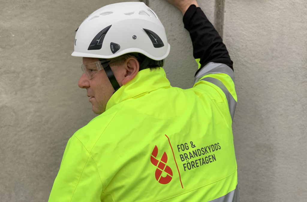 En arbetare i gul skyddsjacka och vit hjälm står vänd mot en vägg och markerar hur ny utbildning ska möta kompetensbristen på fog- och brandtätare.