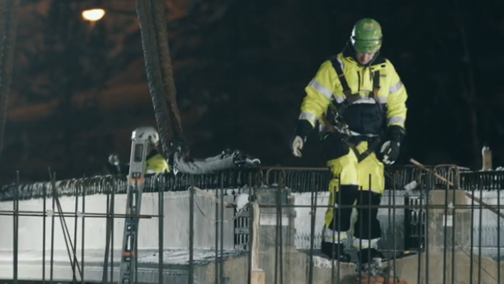 Byggnadsarbetare i skyddsutrustning, del av Från snabbmat till byggbranschen - Nationell yrkesutbildning, går på en snöig, ofärdig byggnadsstruktur på natten.