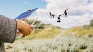 En person opererar en drönare med fjärrkontroll och surfplatta utomhus under blå himmel - idealisk utbildning för Företagsutbildning - UAS fjärrpilot och operatör inom kategori specifik.