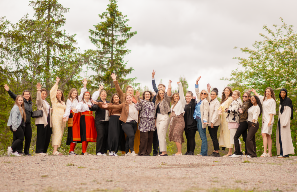 En grupp människor står utomhus på grus, ler och sträcker upp armarna, firar sin examen som Affärsutvecklare inom besöksnäringen.