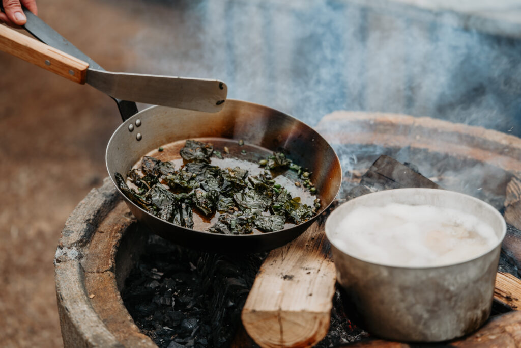 En stekpanna med sauterade grönsaker och en kastrull med kokande vatten över en utomhuseld – smaker inspirerade av allt från kryddfält i Skåne till tång i Bohuslän.