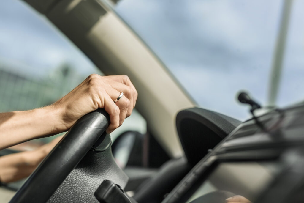 Närbild på en persons hand på en bilratt, med solljus som strilar in genom fönstret – i samarbete med trafikskolan My Driving Academy Sweden AB.