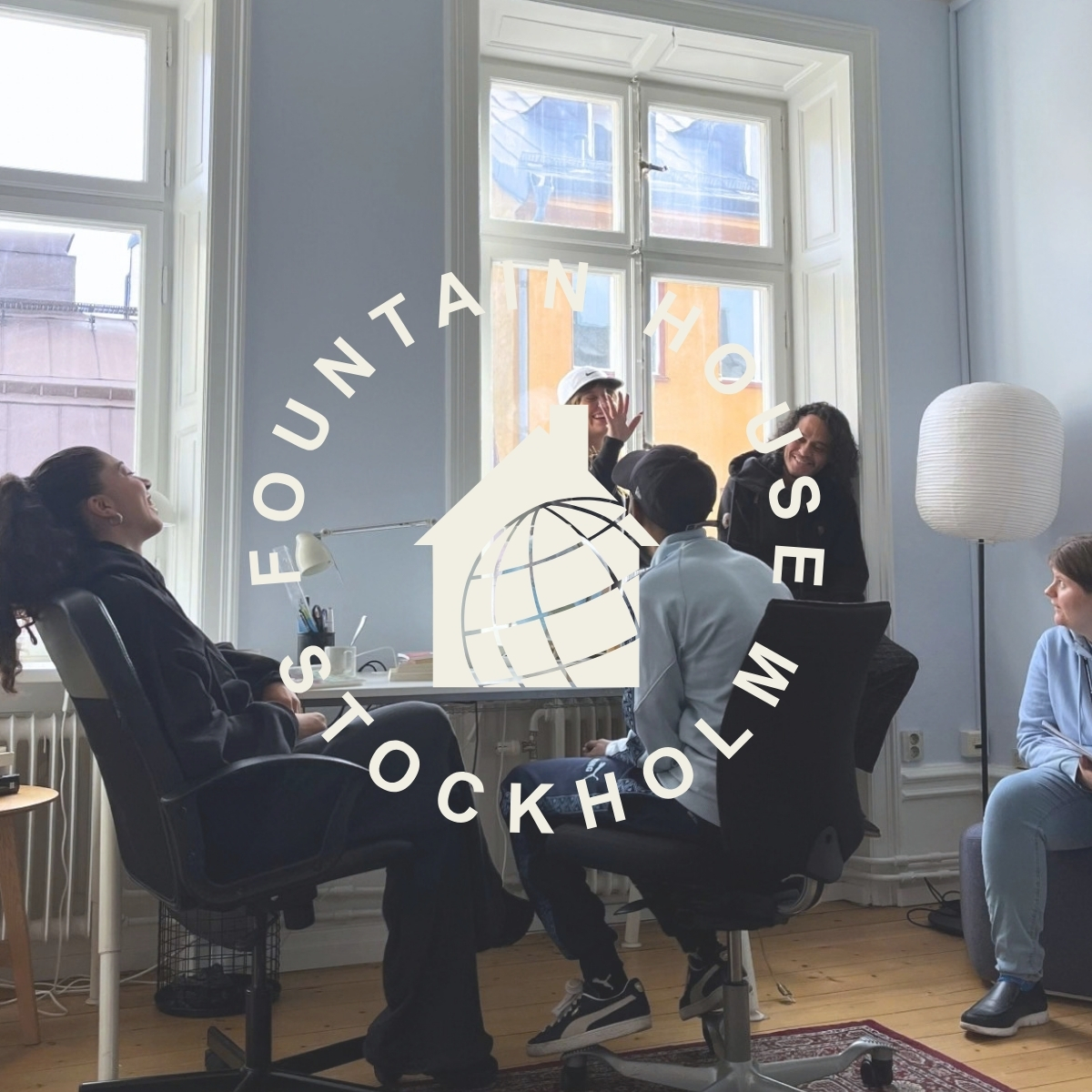 Fyra personer sitter och pratar i ett ljust rum med stora fönster och en golvlampa; en logotyp syns över bilden.