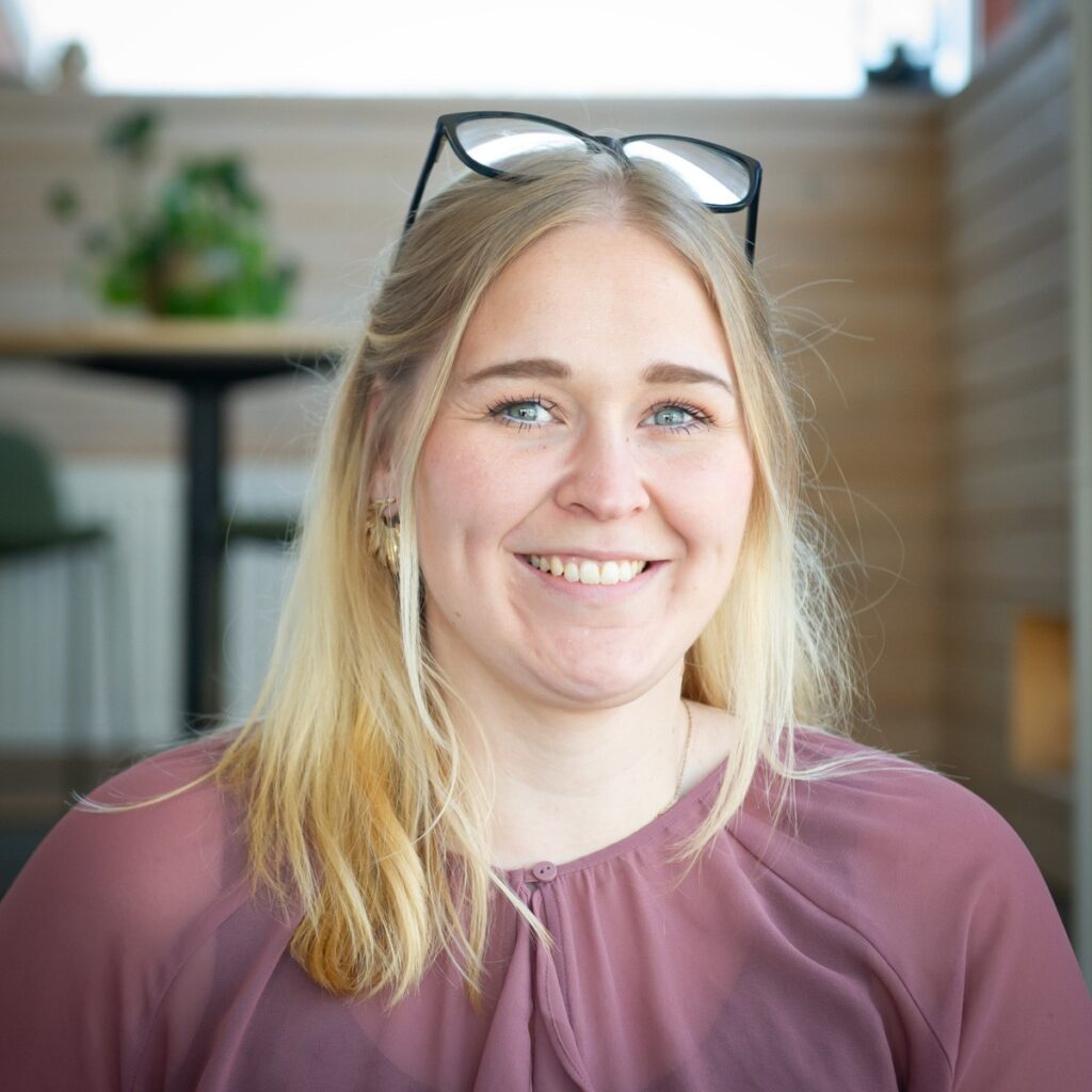 En leende blond kvinna med glasögon på huvudet – från kulturbranschen till tunga maskiner.